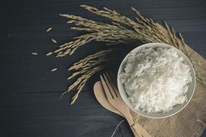 Cooked rice with dry rice and ears of jasmine rice on wooden table photo