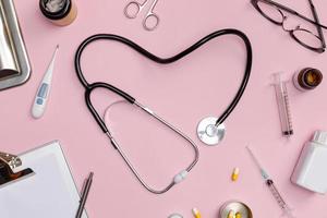 Stethoscope in shape of heart with medical documents, thermometer, syringe and pills on pink table background, Good health from Doctor concept, Top view with copy space, Isolated on pink photo