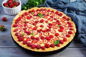 Delicious homemade tart with strawberries and raspberries garnished mint leaves on wooden background photo