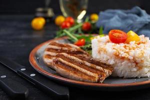 Rice with grilled pork meat, tomatoes and green herbs on dark background photo