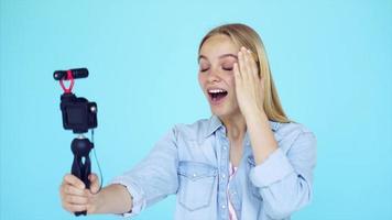 Vlogger uses camera and selfie stick to record video blog in front of a blue background