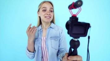 Vlogger uses camera and selfie stick to record video blog in front of a blue background