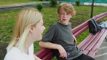 Teenage boy and girl hanging out at the park with a skateboard video