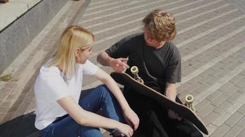 Teenage boy and girl hanging out at the park with a skateboard video