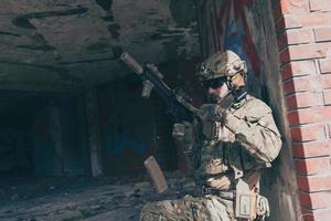 un soldado barbudo con uniforme de las fuerzas especiales en una peligrosa misión militar, vuelve a archivar su arma mientras se esconde de la pared. enfoque selectivo foto