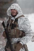 Winter war in the Arctic mountains. Operation in cold conditions.Soldier in winter camouflaged uniform in Modern warfare army on a snow day on forest battlefield with a rifle. Selective focus photo