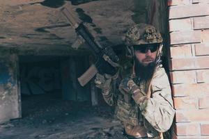 un soldado barbudo con uniforme de las fuerzas especiales en una peligrosa misión militar, vuelve a archivar su arma mientras se esconde de la pared. enfoque selectivo