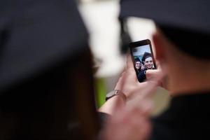 group of happy international students in mortar boards and bachelor gowns with diplomas taking selfie by smartphone photo