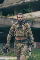 un soldado barbudo con uniforme de las fuerzas especiales camina por un edificio abandonado después de una misión exitosa. enfoque de selección foto