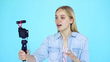 Vlogger uses camera and selfie stick to record video blog in front of a blue background