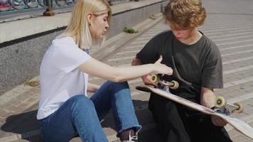 adolescenziale ragazzo e ragazza sospeso su a il parco con un' skateboard video