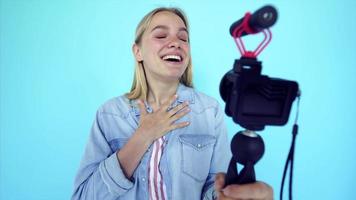 Vlogger uses camera and selfie stick to record video blog in front of a blue background