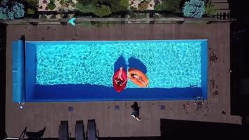vue aérienne d'une piscine avec des femmes sur des flotteurs rouge vif et orange