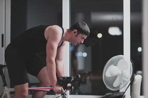 hombre en bicicleta en el entrenador de la máquina que está haciendo ejercicio en el hogar por la noche jugando al juego de carreras de bicicletas en línea foto