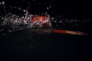 atleta de triatlón nadando en la noche oscura con traje de neopreno foto