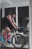 hombre en bicicleta en el entrenador de la máquina que está haciendo ejercicio en el hogar por la noche jugando al juego de carreras de bicicletas en línea