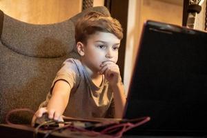 Pensive kid e-leaning over laptop from home. photo