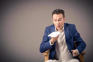 Sick businessman using tissue while sneezing against the wall. photo