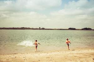 Rear view of kids having fun and running on the beach in summer day. photo