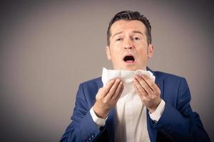 Businessman sneezing in tissue while suffering from allergy. photo