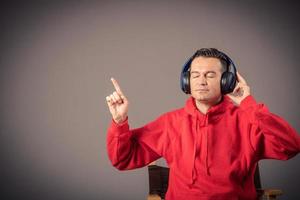 Portrait of man with headphones listening music with eyes closed and pointing at copy space on wall. photo