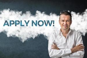 Apply now. Confident businessman with arms crossed standing next to sign on the wall. Job search concept. photo