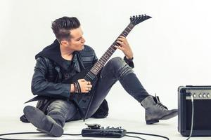 Hard rock musician playing electric guitar while sitting on the floor. photo