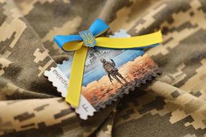 TERNOPIL, UKRAINE - SEPTEMBER 2, 2022 Famous Ukrainian postmark with russian warship and ukrainian soldier as wooden souvenir on army camouflage uniform photo