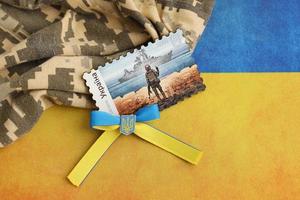 TERNOPIL, UKRAINE - SEPTEMBER 2, 2022 Famous Ukrainian postmark with russian warship and ukrainian soldier as wooden souvenir on army camouflage uniform and national flag photo