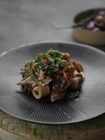 Close-up view angle of Indonesian traditional spicy stir fry squid, top with green chillies, on a black plate and uneven color grey table. photo