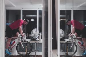 hombre en bicicleta en el entrenador de la máquina que está haciendo ejercicio en el hogar por la noche jugando al juego de carreras de bicicletas en línea