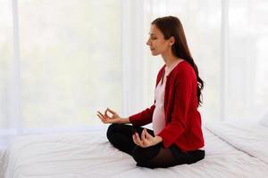 la mujer embarazada se sienta en la cama en su dormitorio meditando sola en paz y felicidad. la nueva madre descansando sentándose para relajarse. foto