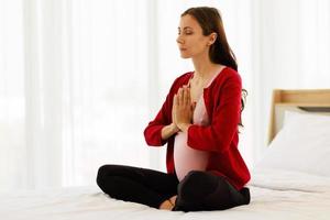 la mujer embarazada se sienta en la cama en su dormitorio meditando sola en paz y felicidad. la nueva madre descansando sentándose para relajarse. foto