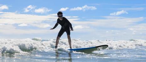 Young boy wearing swimming goggles stable stands on soft board while practicing surfing in beginner's class. photo