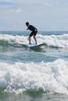 un joven con gafas de natación se para estable en una tabla blanda mientras practica surf en la clase de principiantes. foto