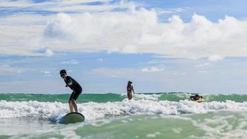 Young boy wearing swimming goggles stands on soft board while practicing surfing in beginner's class. photo