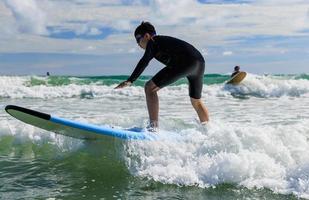 Young boy wearing swimming goggles stands on soft board while practicing surfing in beginner's class. photo