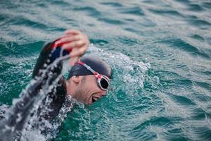 triathlon athlete swimming on lake in sunrise  wearing wetsuit photo