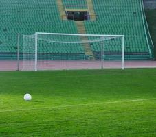 Soccer ball on grass at goal and stadium in background photo