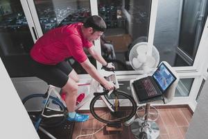 Man cycling on the machine trainer he is exercising in the home at night playing online bike racing game photo