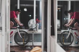 hombre en bicicleta en el entrenador de la máquina que está haciendo ejercicio en el hogar por la noche jugando al juego de carreras de bicicletas en línea foto