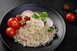 Quinoa salad with vegetables, raspberry and tomatoes on the black table. Super food for healthy and concept of balanced diet photo