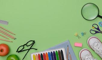 Creative flatlay of education green table with student books, shoes, colorful crayon, eye glasses, empty space isolated on green background, Concept of education and back to school photo