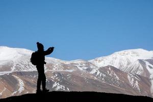 Tourist with backpack taking a photo on the rock in the beautiful mountains view of snowy Tso Moriri Lake in Leh Ladakh india, freedom concept