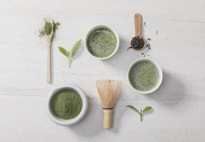 polvo de té verde matcha orgánico en un tazón con batidor de alambre y hoja de té verde sobre una mesa de piedra blanca, producto orgánico de la naturaleza para la salud con estilo tradicional foto