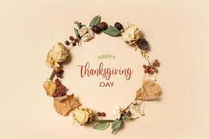 composición de otoño con feliz texto de saludo del día de acción de gracias. corona hecha de hojas secas y flores sobre fondo beige pastel foto