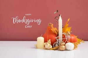 Autumn composition with Happy Thanksgiving Day greeting text. Dried leaves, pumpkins and candles on white pink background photo