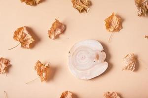 Autumn composition. Pattern made of dried leaves and wooden saw on pastel beige background for cosmetic presentation. Autumn, fall concept. Flat lay, top view photo