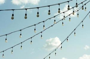 bombillas blancas económicas colgadas en fila. vista de bombillas contra el cielo. foto