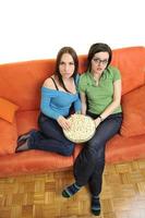 amigas comiendo palomitas de maíz y viendo la televisión en casa foto